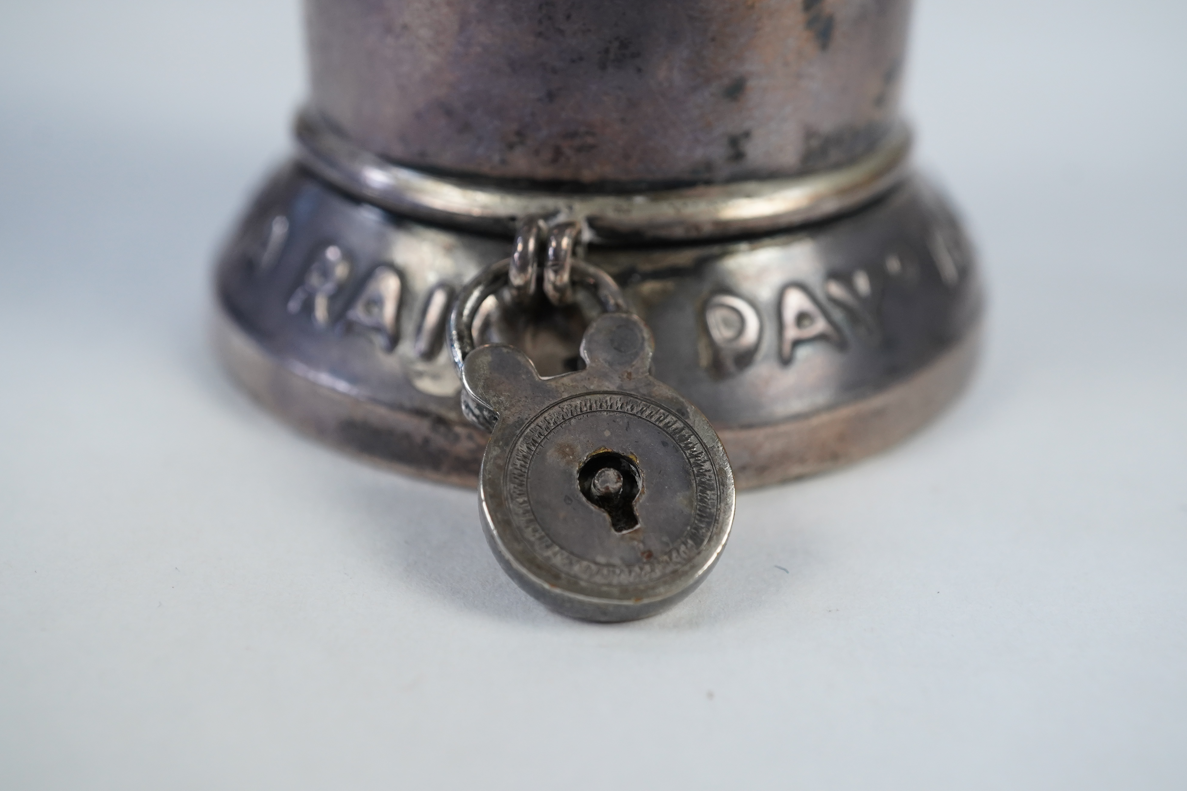 A matched pair of George V novelty silver money boxes, each cylindrical box embossed as a banker with an umbrella, the circular base inscribed 'Always be prepared for a rainy day'